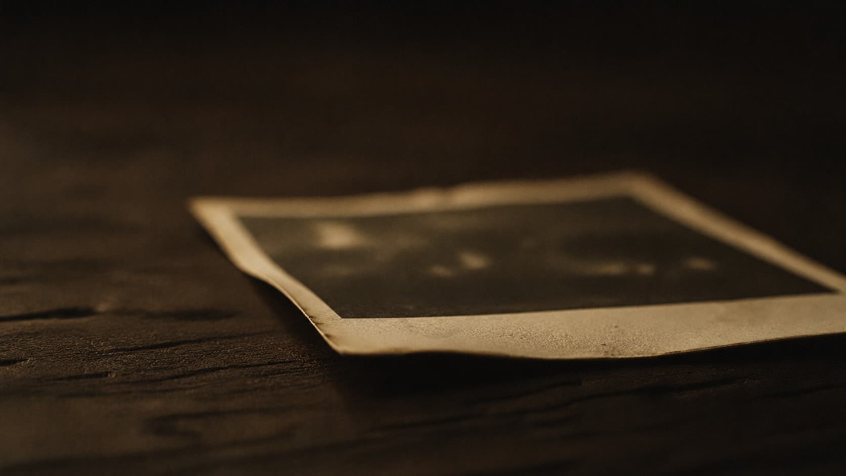 An old photograph face-down on a wooden surface, warm dim light.